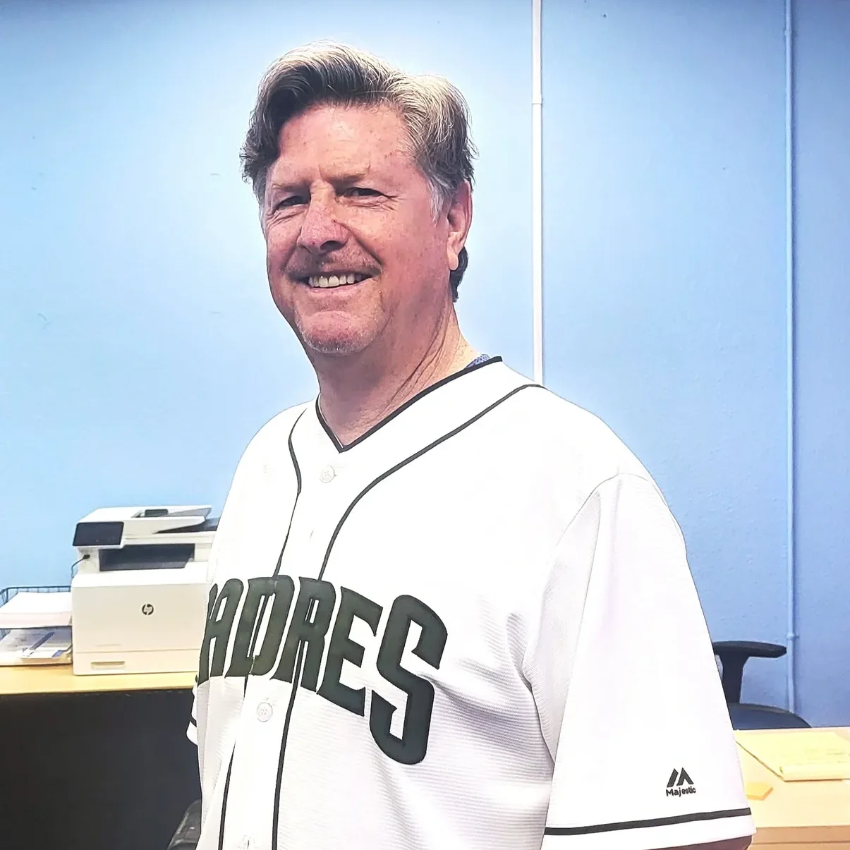 A man in a baseball uniform standing next to a desk.